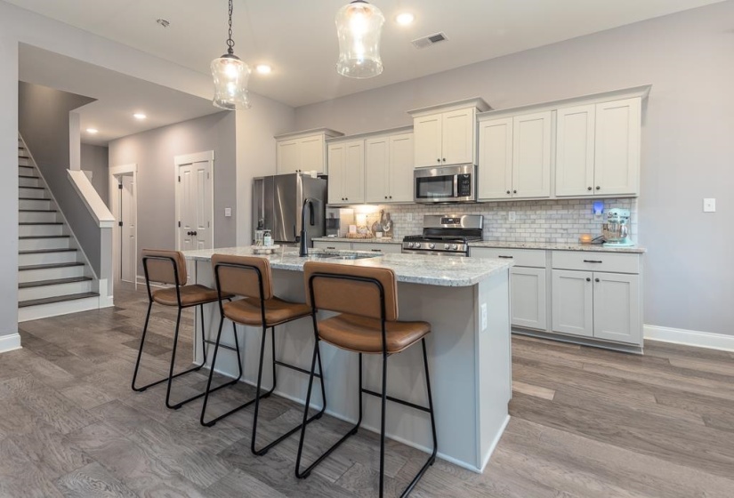 Kitchen featuring light stone countertops, appliances with stainless steel finishes, hanging light fixtures, a breakfast bar, and decorative backsplash