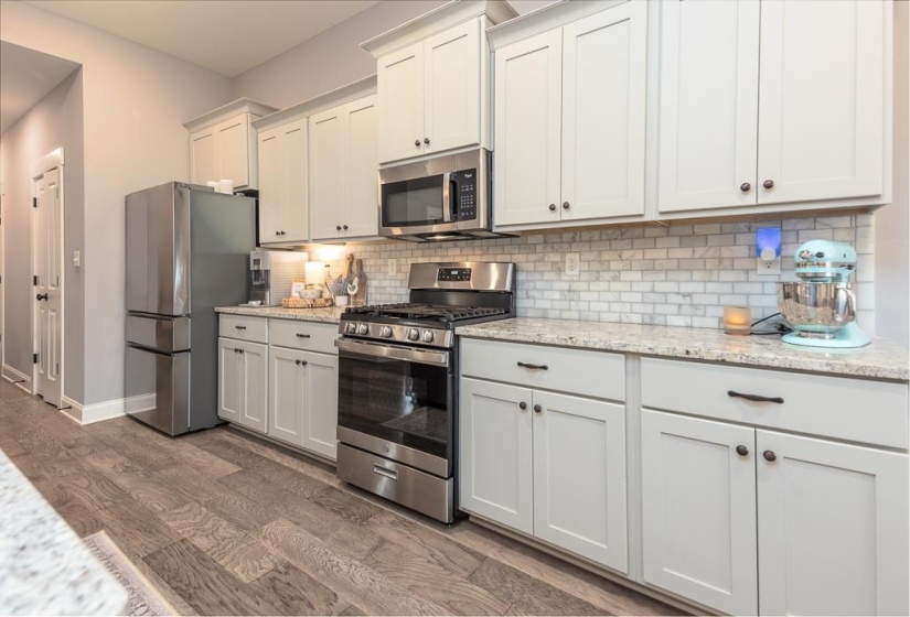 Kitchen featuring appliances with stainless steel finishes, light stone countertops, white cabinetry, dark wood finished floors, and tasteful backsplash
