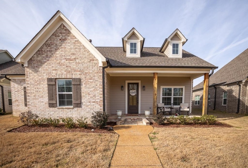 View of front of property with covered porch, a front lawn, roof with shingles, and brick siding
