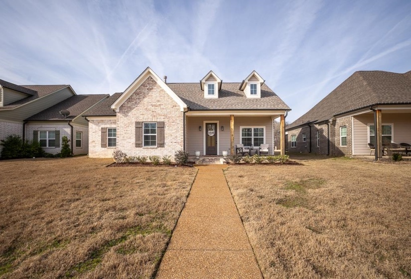 View of front of house with a shingled roof, covered porch, a front lawn, and brick siding
