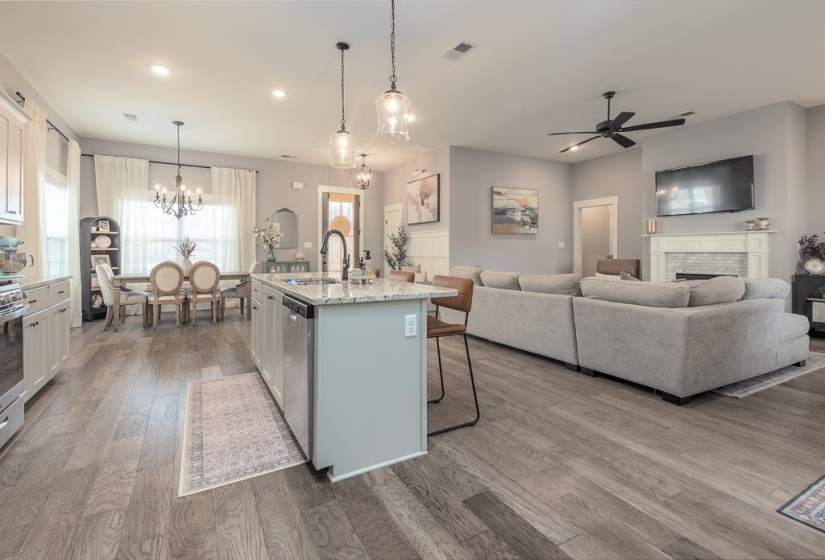 Kitchen featuring decorative light fixtures, an island with sink, a kitchen bar, light stone countertops, and light wood-style floors