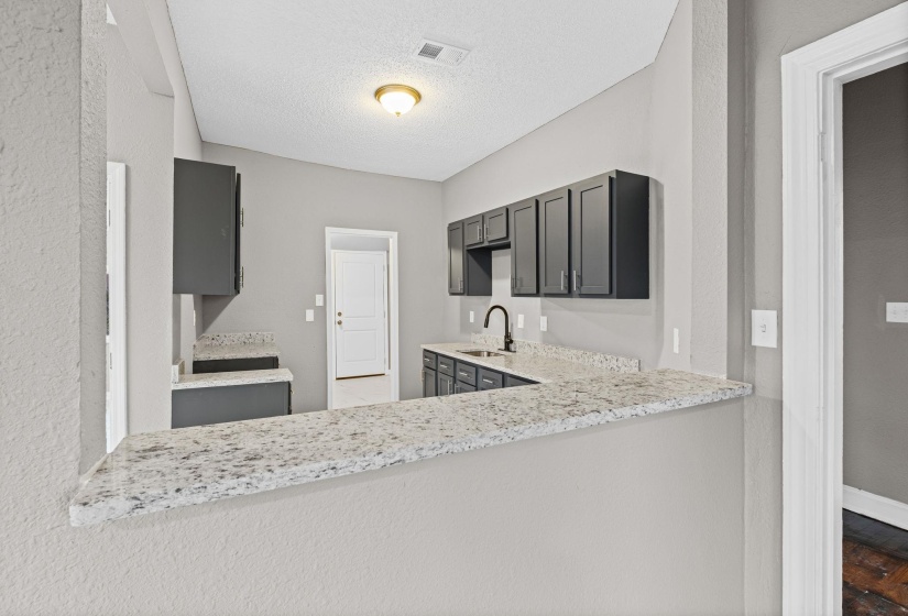 Kitchen with light stone counters, a textured ceiling, gray cabinetry, and a peninsula