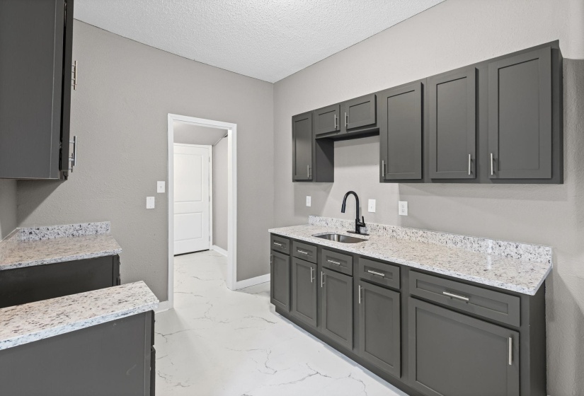 Kitchen with light stone counters, light marble finish floors, gray cabinets, and a textured ceiling