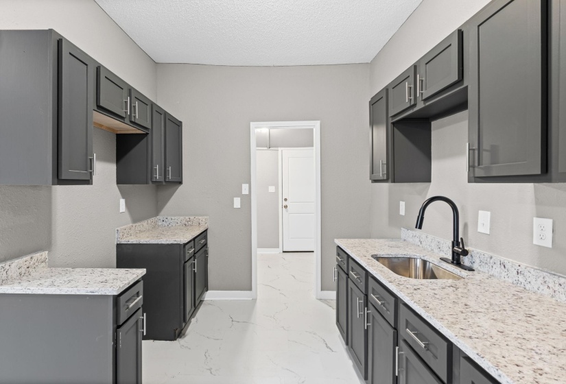 Kitchen featuring gray cabinetry, light stone counters, light marble finish flooring, and a textured ceiling