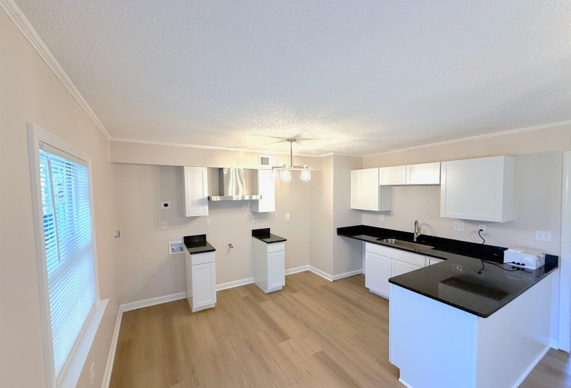 Kitchen featuring white cabinetry, hanging light fixtures, a textured ceiling, crown molding, and a peninsula