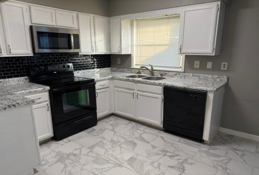 Kitchen with black appliances, white cabinetry, light marble finish flooring, and tasteful backsplash