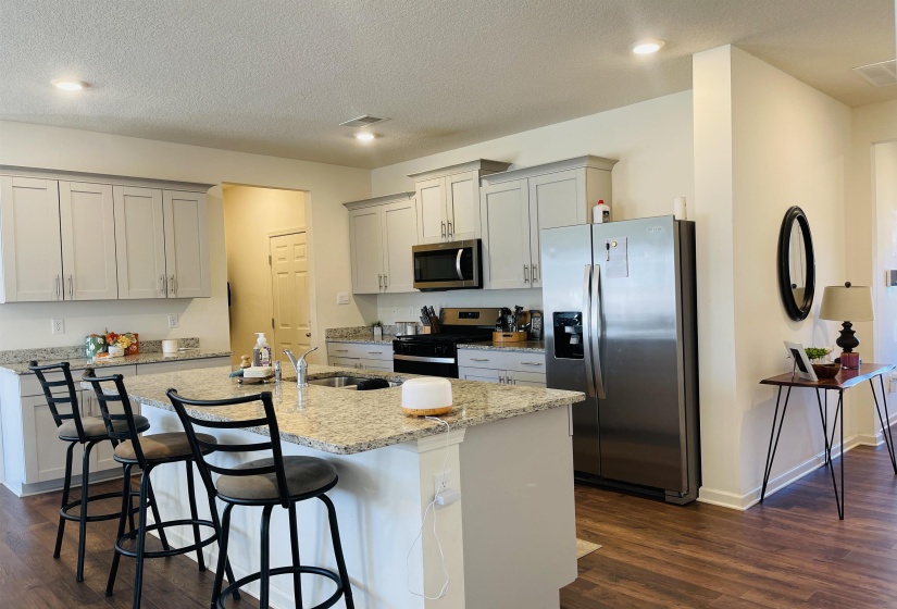 Kitchen with appliances with stainless steel finishes, light stone countertops, dark wood finished floors, a breakfast bar, and a textured ceiling