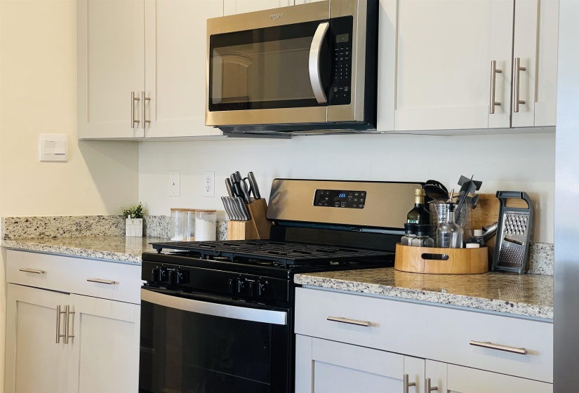 Kitchen featuring gas range, stainless steel microwave, white cabinetry, and light stone countertops