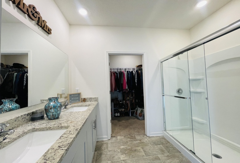 Bathroom featuring a spacious closet, double vanity, a shower stall, and stone finish flooring