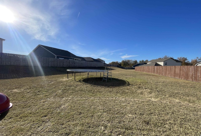 Fenced backyard featuring a trampoline