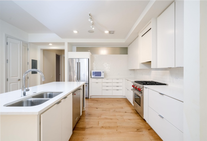 Kitchen featuring white cabinets, modern cabinets, high quality appliances, decorative backsplash, and light wood finished floors