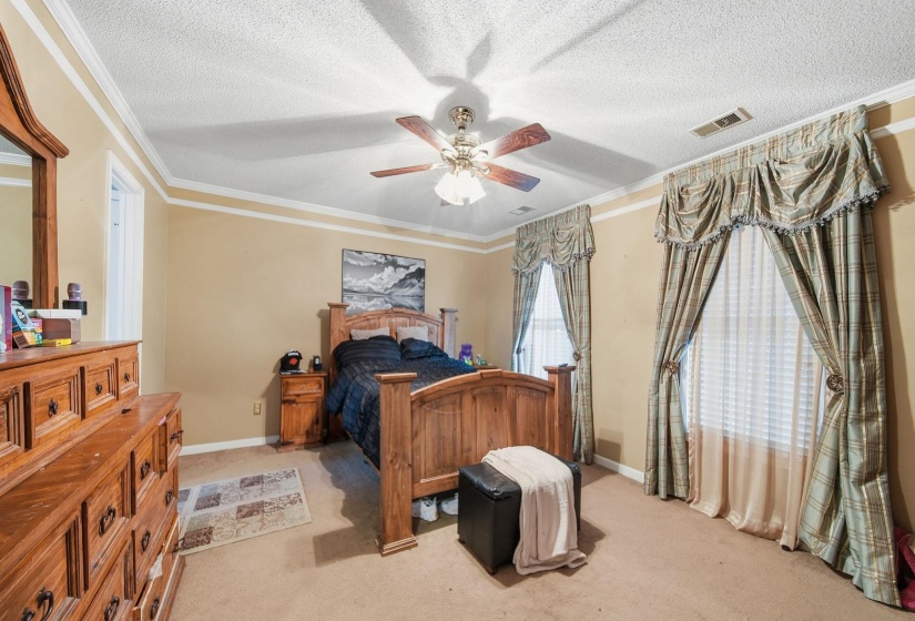 Bedroom featuring ornamental molding, light carpet, ceiling fan, and a textured ceiling