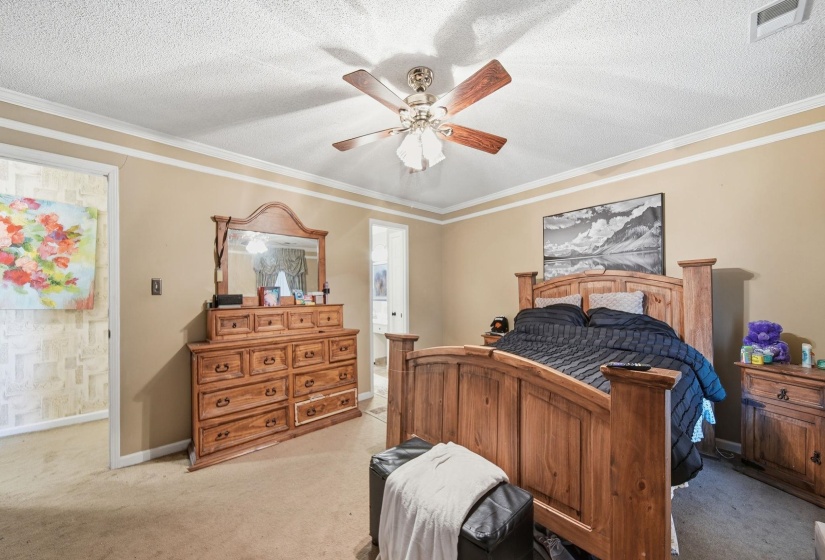 Bedroom featuring a textured ceiling, crown molding, light carpet, ceiling fan, and ensuite bathroom