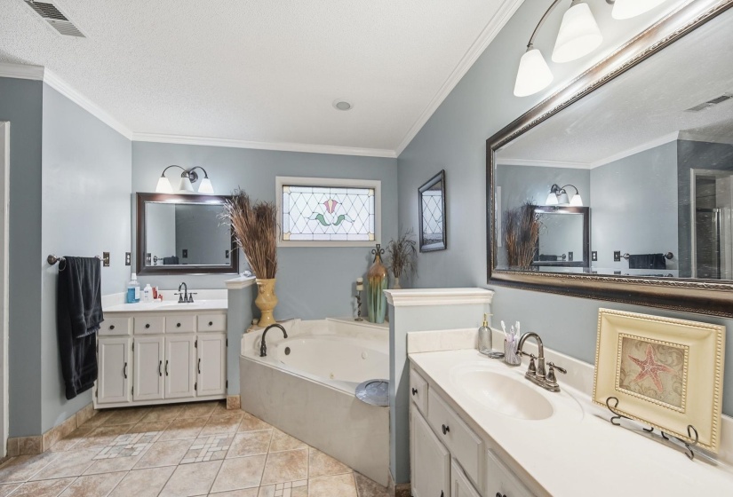 Bathroom featuring two vanities, a whirlpool tub, crown molding, light tile patterned flooring, and a textured ceiling