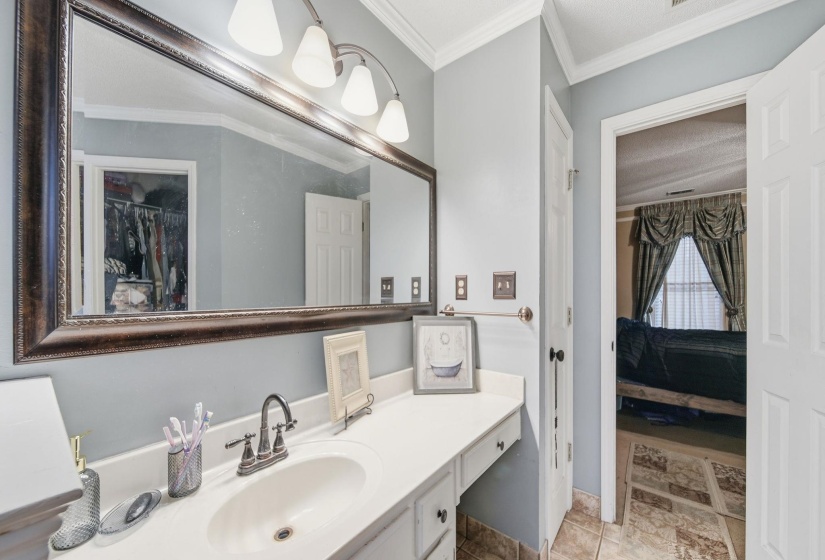 Ensuite bathroom with ornamental molding, vanity, and a walk in closet