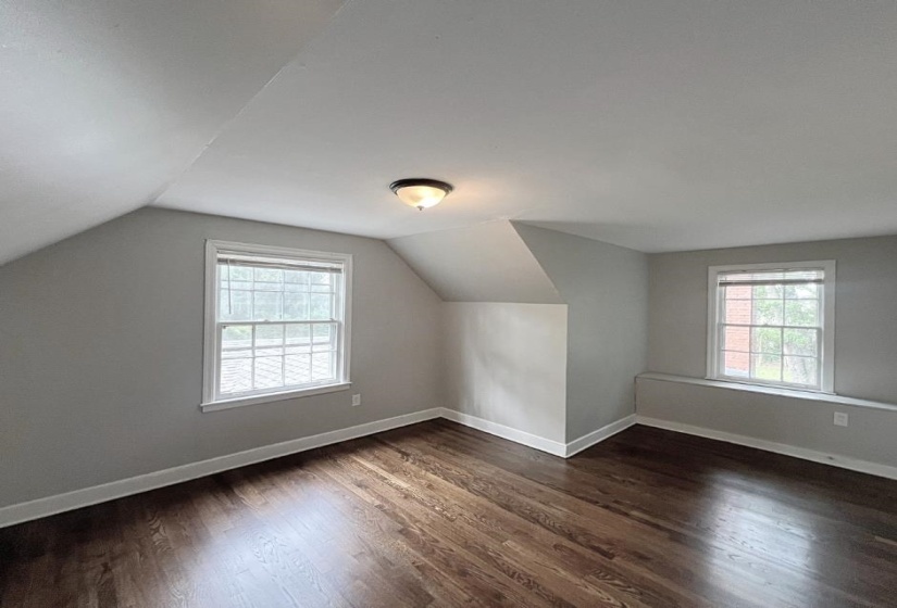 Additional living space with dark wood-style floors, vaulted ceiling, and baseboards