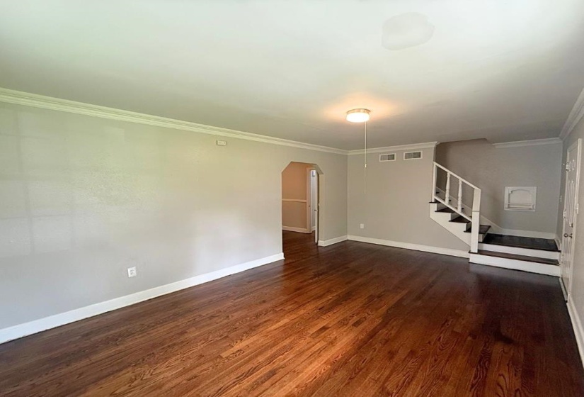 Empty room with arched walkways, wood finished floors, baseboards, stairs, and ornamental molding