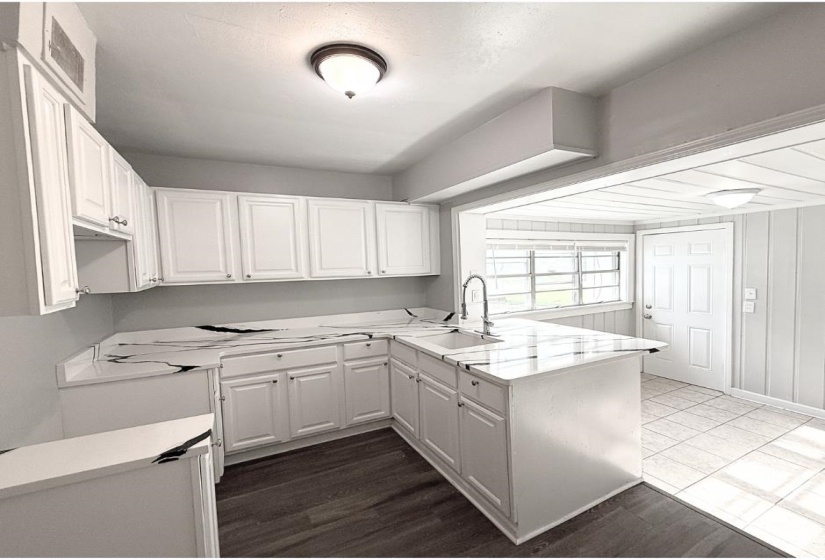 Kitchen with a sink, a peninsula, light countertops, and white cabinets