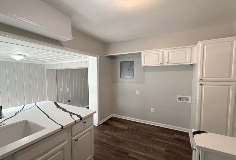Kitchen with electric panel, dark wood-style flooring, light countertops, baseboards, and white cabinetry