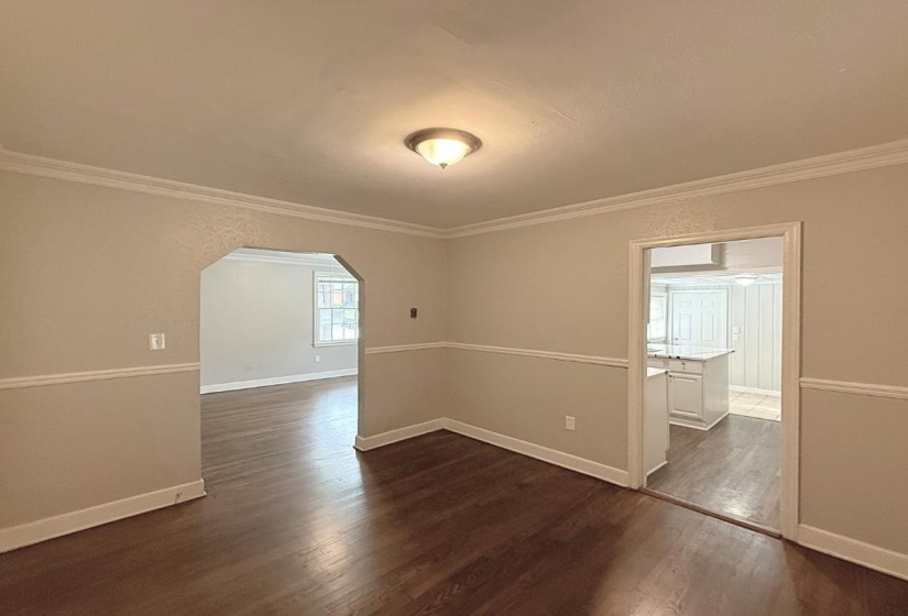 Empty room featuring arched walkways, dark wood-type flooring, ornamental molding, and baseboards