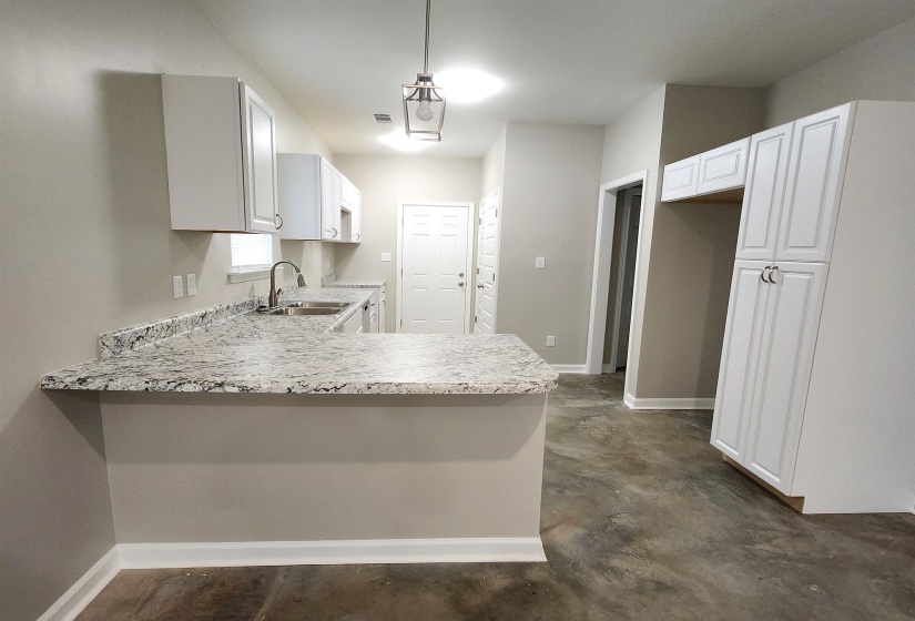 Kitchen featuring light countertops, a peninsula, concrete flooring, and white cabinetry
