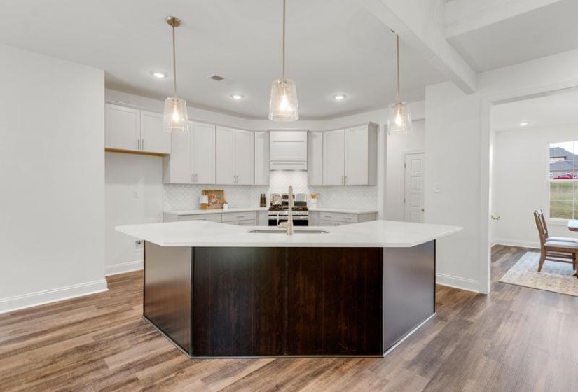 Kitchen with white cabinetry, backsplash, pendant lighting, dark wood-style floors, and a center island with sink