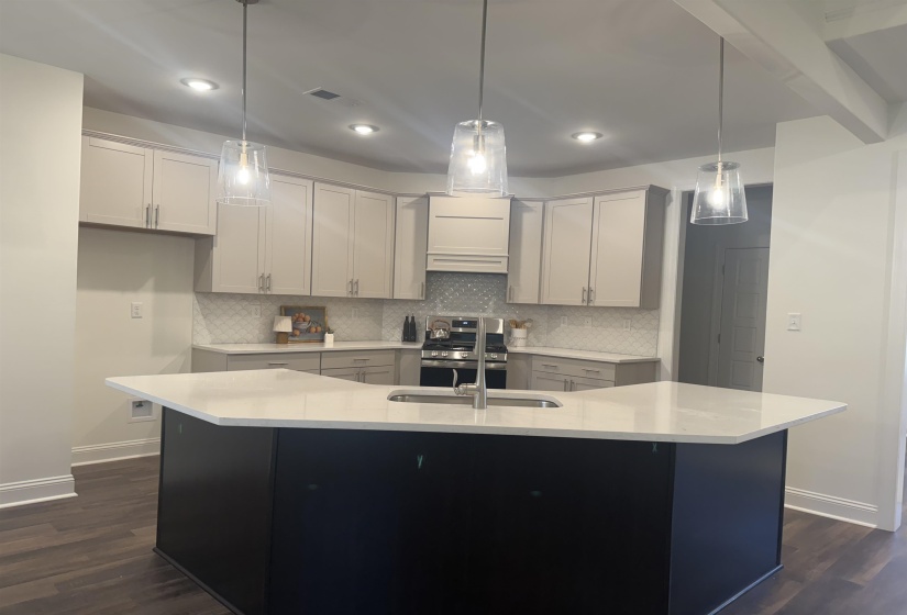 Kitchen with pendant lighting, gas stove, backsplash, dark wood finished floors, and an island with sink