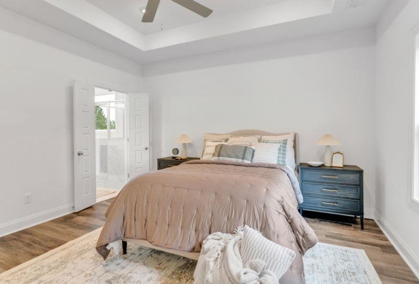 Bedroom featuring a raised ceiling, wood finished floors, a ceiling fan, and ensuite bath