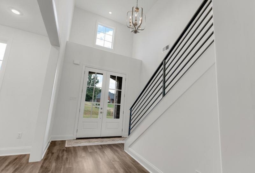 Foyer entrance with french doors, wood finished floors, a chandelier, stairs, and a towering ceiling