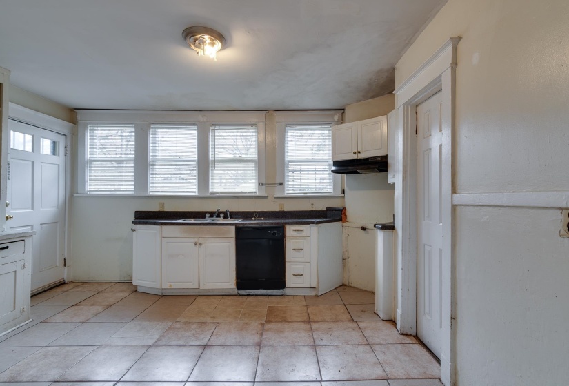 Kitchen with white cabinets, dark countertops, dishwasher, under cabinet range hood, and light tile patterned floors