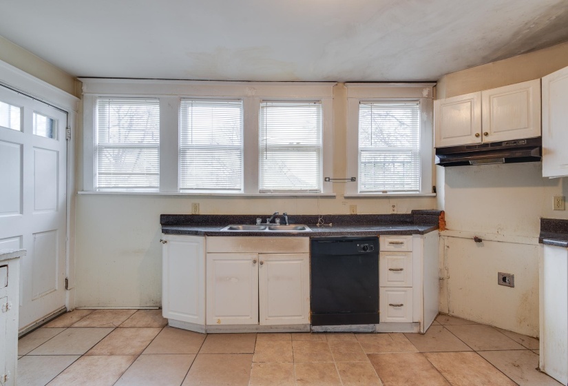 Kitchen featuring white cabinets, dishwasher, dark countertops, under cabinet range hood, and light tile patterned floors