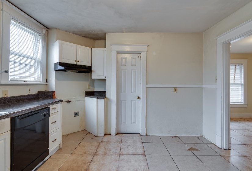 Kitchen featuring black dishwasher, white cabinets, dark countertops, light tile patterned floors, and under cabinet range hood