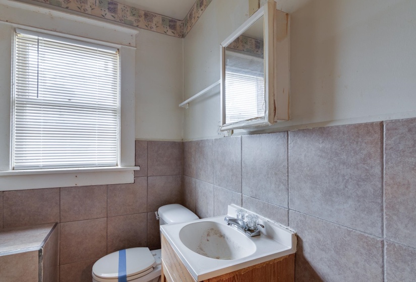 Half bath featuring vanity, tile walls, healthy amount of natural light, and wainscoting