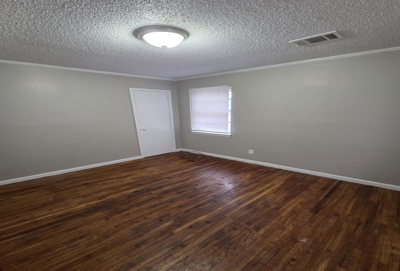 Empty room featuring dark wood-style floors, ornamental molding, and a textured ceiling
