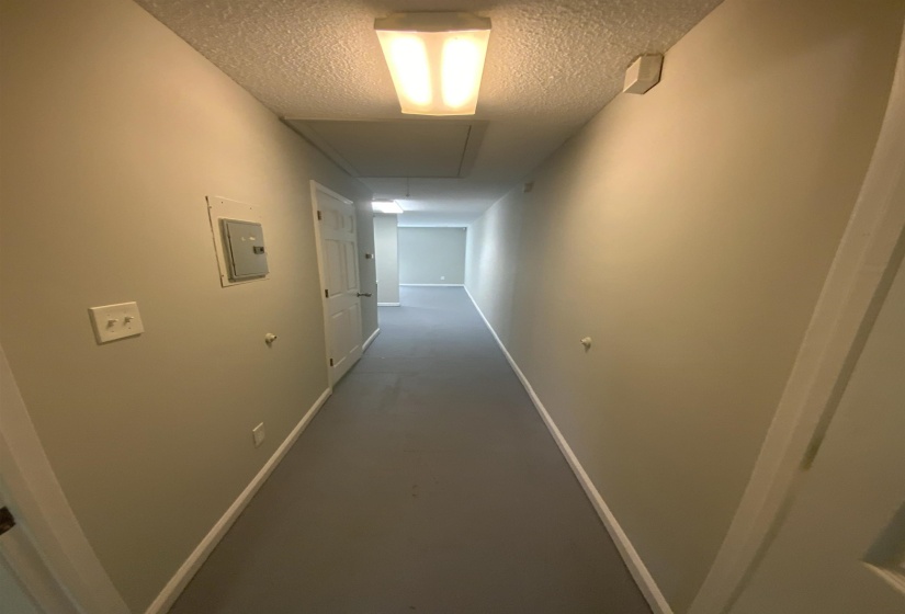 Corridor featuring a textured ceiling, electric panel, finished concrete flooring, and attic access
