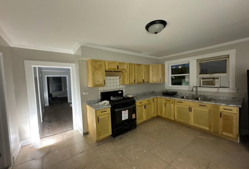 Kitchen with black range with gas stovetop, crown molding, light brown cabinetry, light countertops, and light tile patterned floors