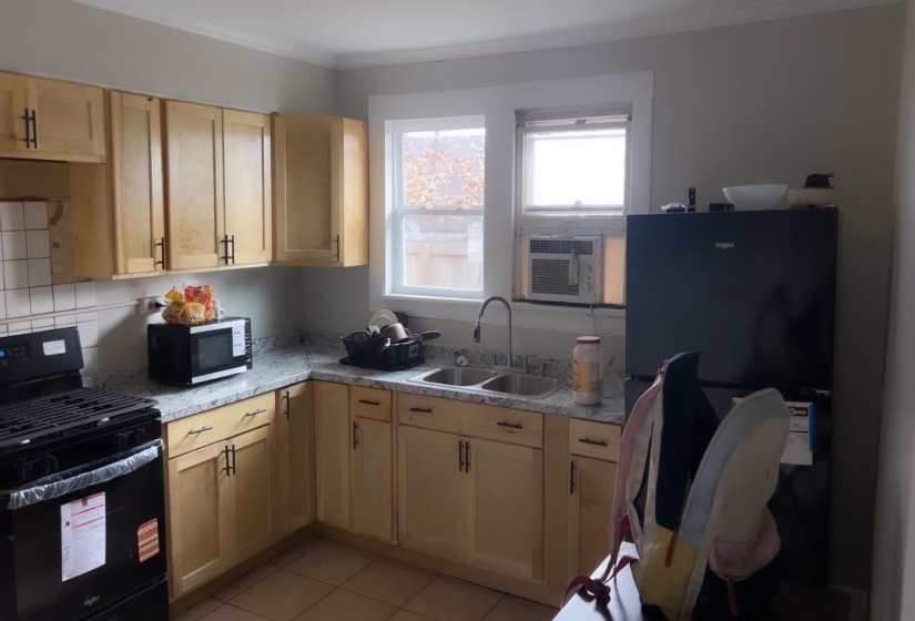 Kitchen with black appliances, light brown cabinetry, light tile patterned floors, and ornamental molding