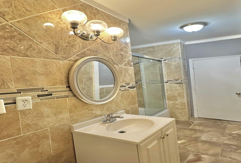 Full bath featuring vanity, tiled shower, tile walls, and crown molding