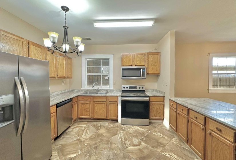Kitchen with stainless steel appliances, hanging light fixtures, a chandelier, light marble finish flooring, and brown cabinetry