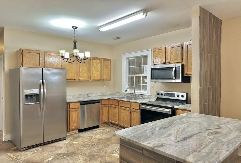 Kitchen featuring stainless steel appliances, hanging light fixtures, a chandelier, and brown cabinetry
