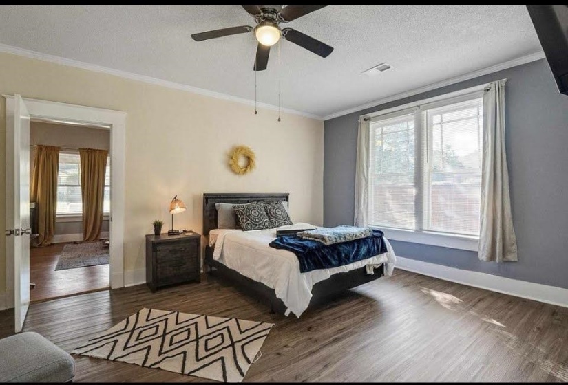 Bedroom featuring wood-finish flooring, a ceiling fan with integrated lighting, and two large windows with white trim