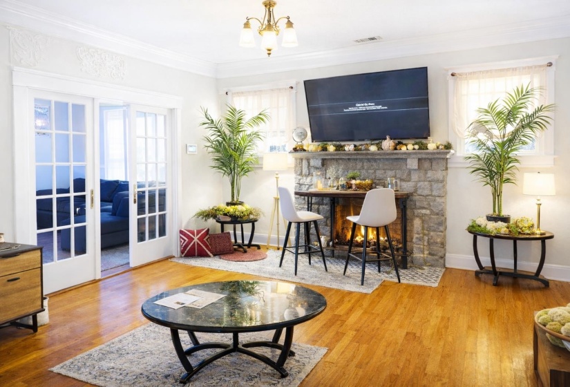 Living space featuring hardwood flooring, a stone-faced fireplace with a mantel, French doors with glass panes, crown molding, and a chandelier