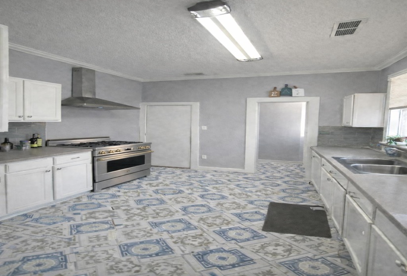 Kitchen featuring decorative patterned flooring, stainless steel range with matching range hood, white cabinetry, and double basin sink