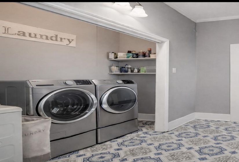 Laundry area featuring patterned tile flooring, light gray walls, built-in shelving, crown molding, and baseboards