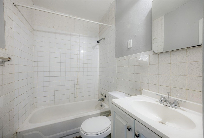Full bathroom featuring tile walls, vanity, shower / bath combination, and a wainscoted wall