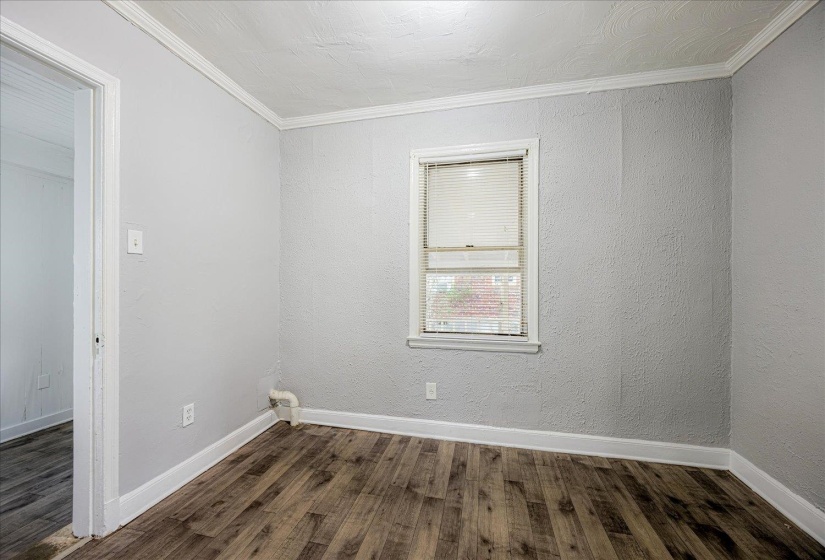 Unfurnished room featuring dark wood finished floors, crown molding, and a textured wall