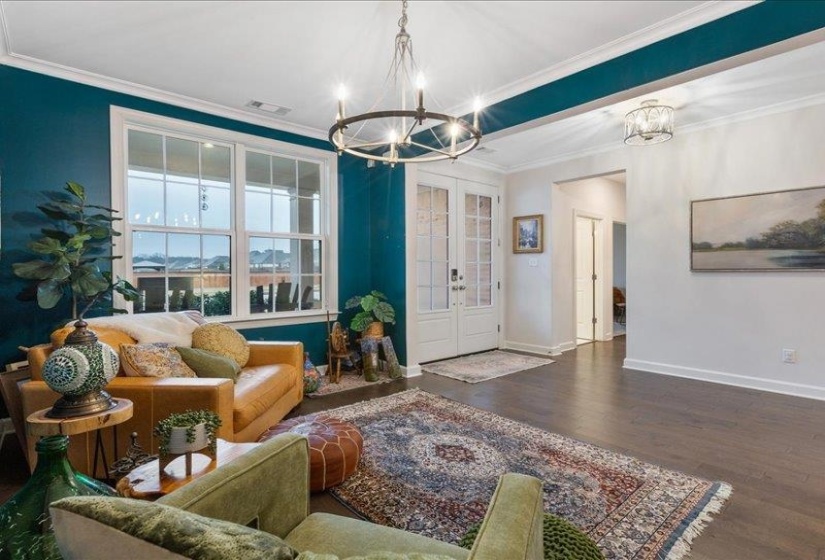 Living area featuring french doors, crown molding, dark wood finished floors, and a chandelier