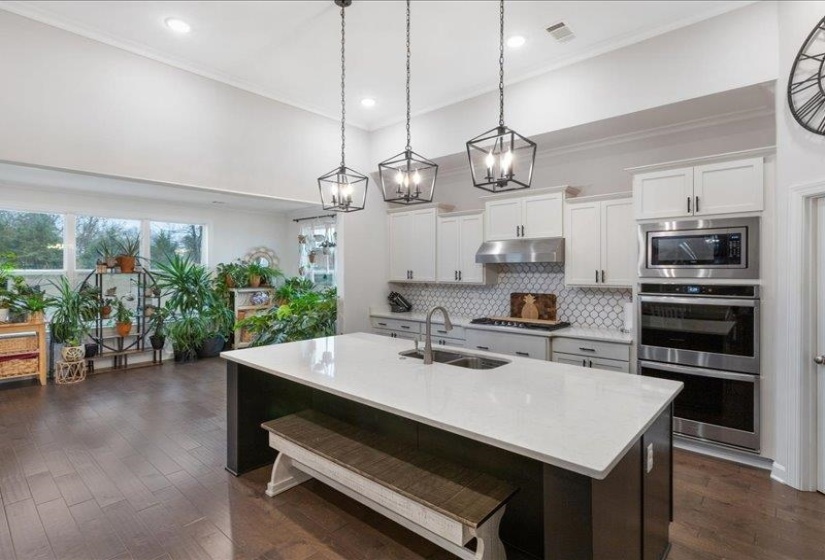 Chef's kitchen featuring hanging light fixtures, oversized quartz island, appliances with stainless steel finishes, double ovens, and ornamental molding