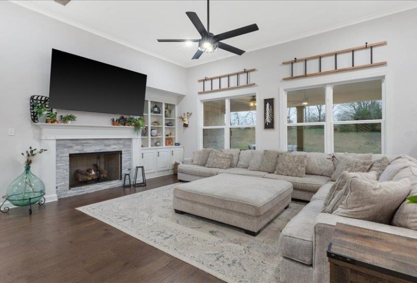Living room featuring crown molding, wood finished floors, a fireplace, ceiling fan, and built in shelves