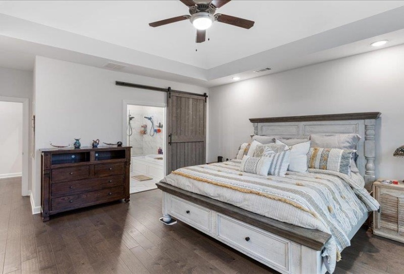 Additional view of primary bedroom generous space, barn door, ceiling fan, dark wood-style floors, recessed lighting, and ensuite bathroom